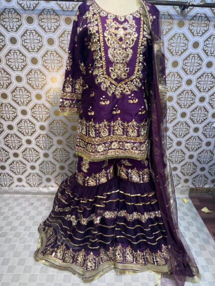 Purple gharara featuring a block print design. The outfit includes a voluminous pair of flared pants and a matching blouse, both adorned with intricate hand-stamped patterns. The rich purple color and detailed print create a vibrant and elegant appearance, ideal for festive occasions.”